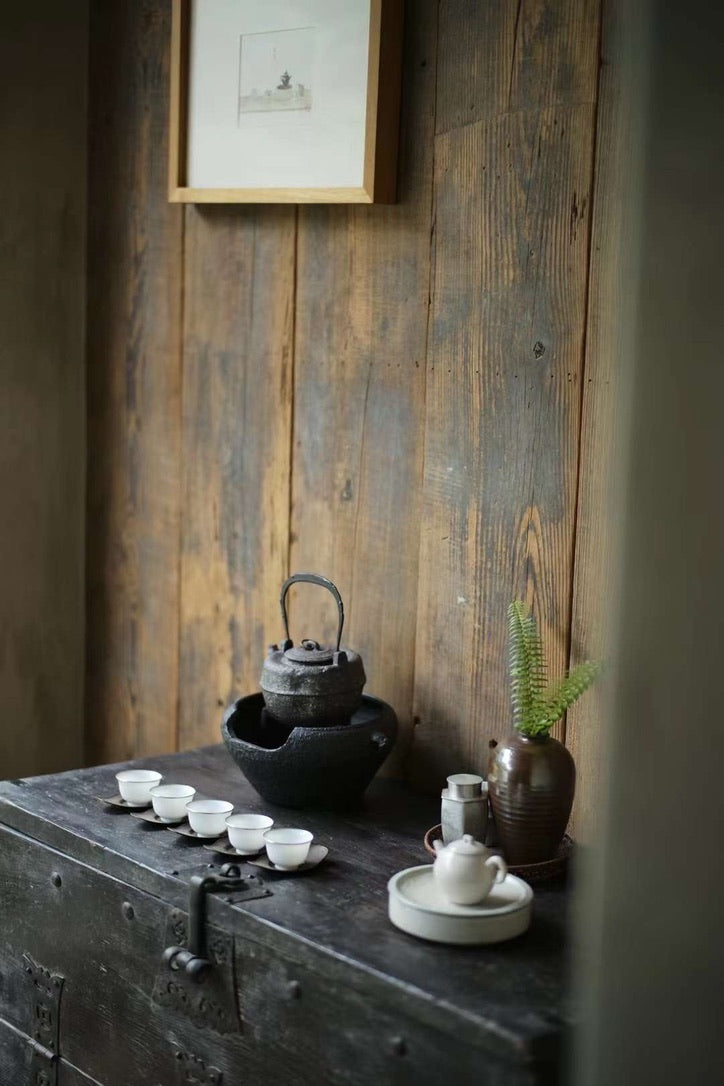A tea set in a rustic setting - tea kettle, tea stove, teacups, and ceramic teapot and hucheng.